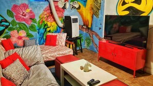 Ein Zimmer mit einer Couch, einem roten Schrank, einem Fernseher und einem Wandgemälde mit Papageien.