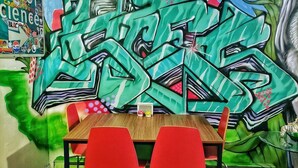 Ein Zimmer mit Wandgemälde aus Graffiti, einem Holztisch und roten Stühlen.