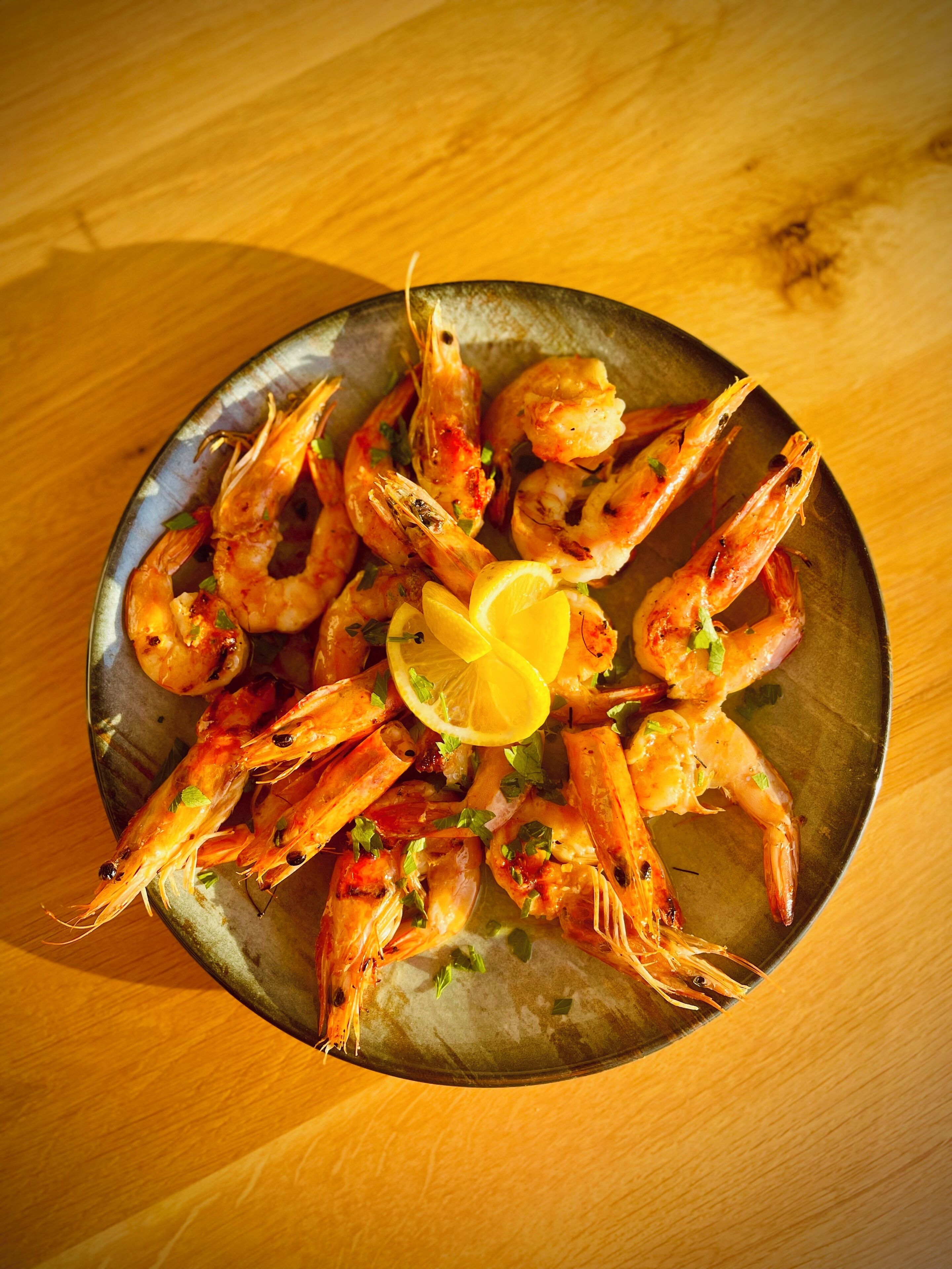 A bowl of cooked shrimp garnished with lemon and herbs.