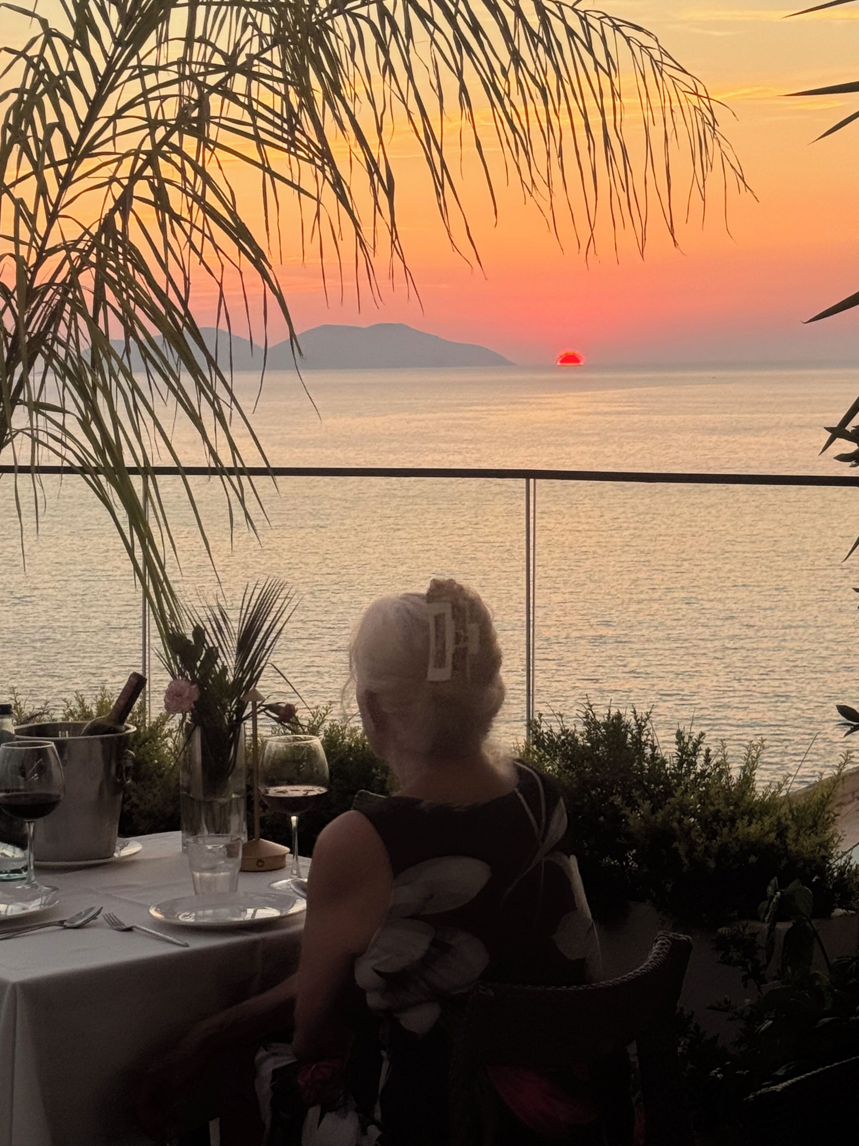 A table set for dining with a view of the sunset over the water.