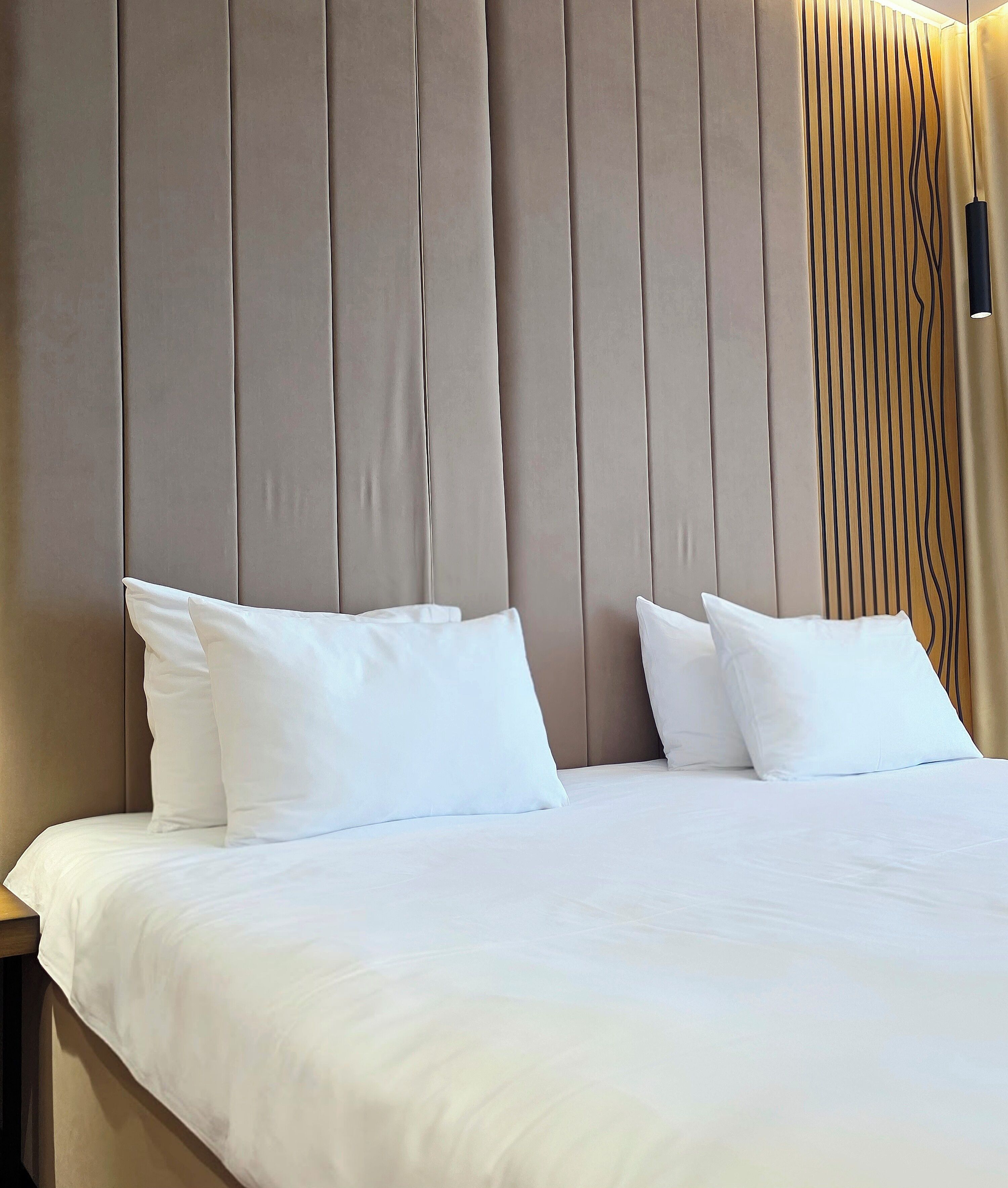 Een bed met witte beddengoed en kussens, een hoofdbord met verticale lijnen, en een hangende lamp.