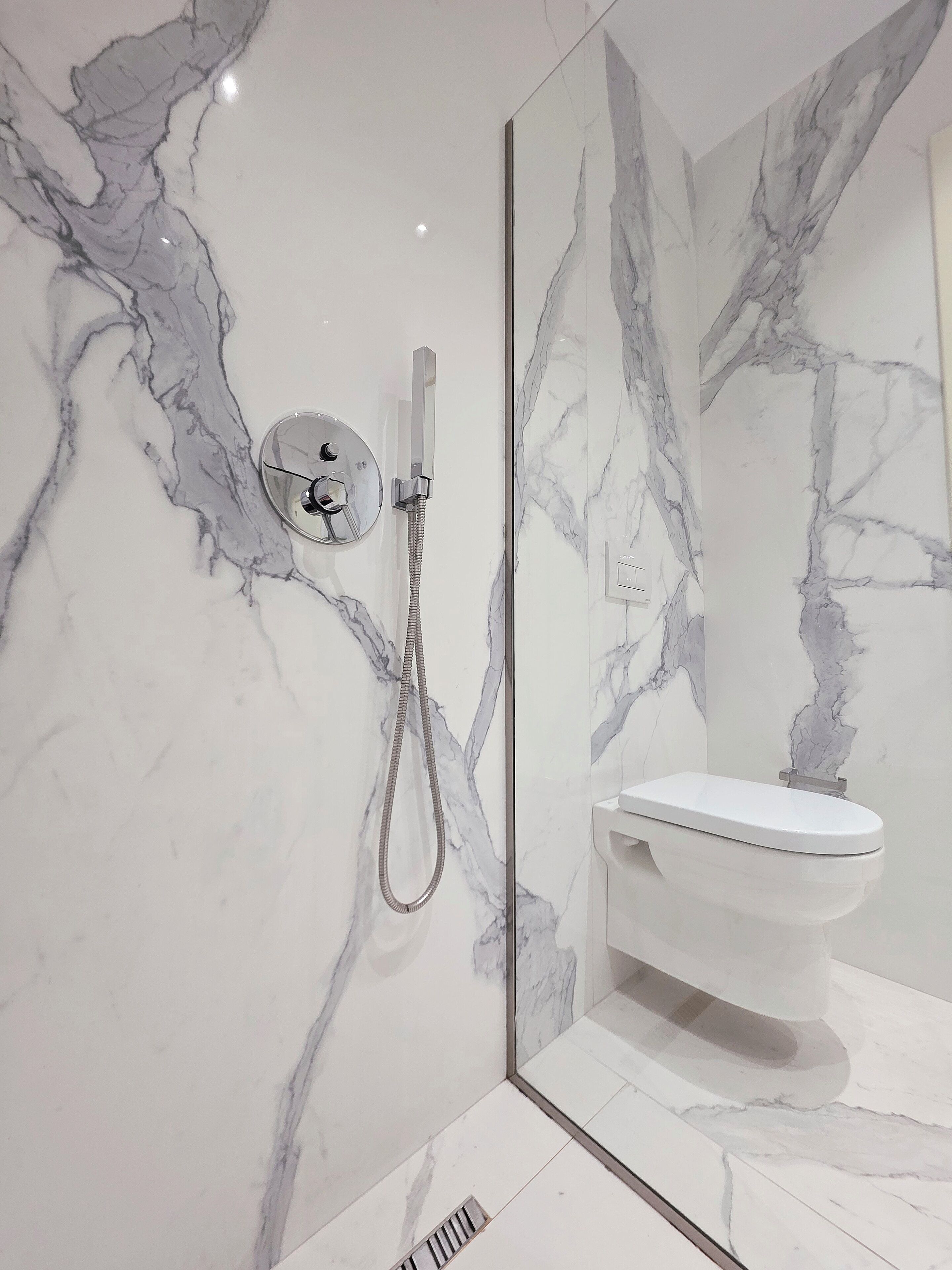 A modern bathroom with a marble wall, a glass-enclosed shower, and a white toilet.