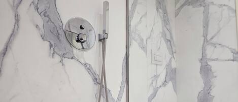A modern bathroom with a marble wall, a glass-enclosed shower, and a white toilet.