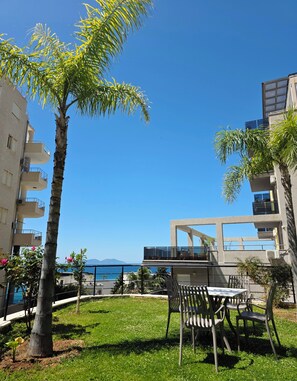 A courtyard with a palm tree, outdoor seating, and a view of the sea. - Valza Boutique Hotel (Vlorë)