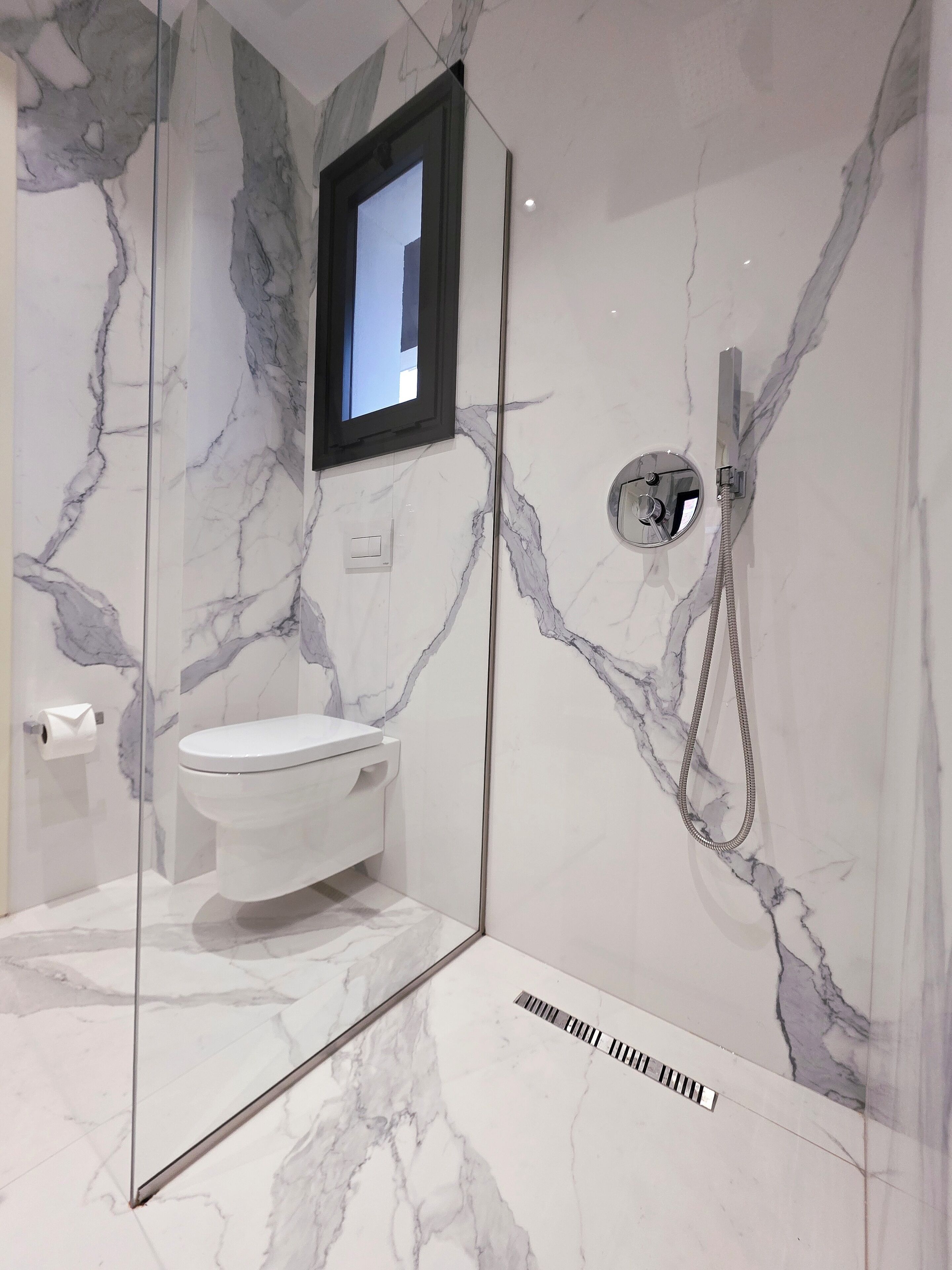 Un baño moderno con ducha envuelta en vidrio, inodoro y pared de mármol.