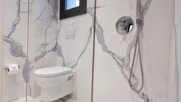 Un baño moderno con ducha envuelta en vidrio, inodoro y pared de mármol.