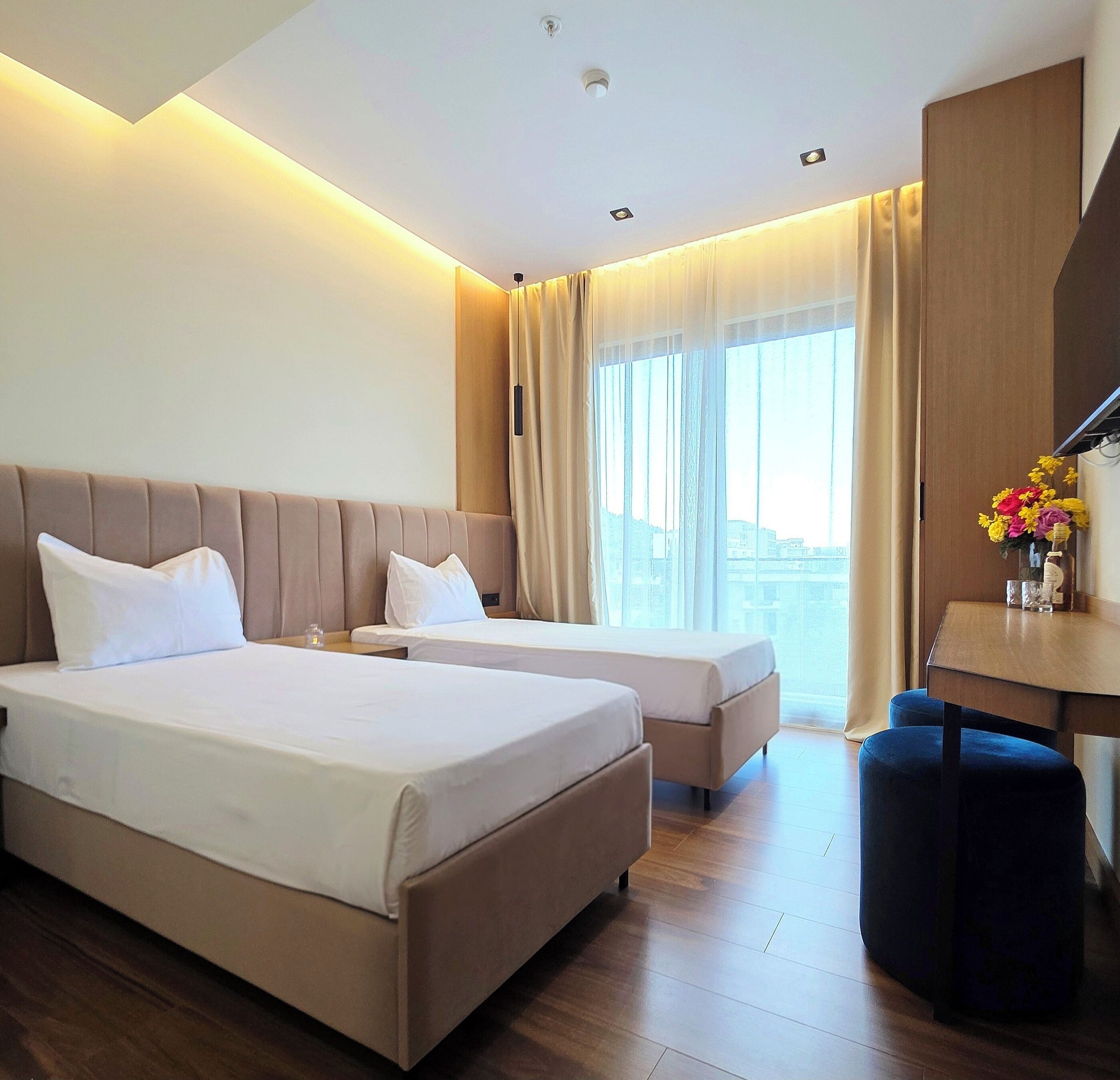 A hotel room with two beds, a desk, and a view of the city.