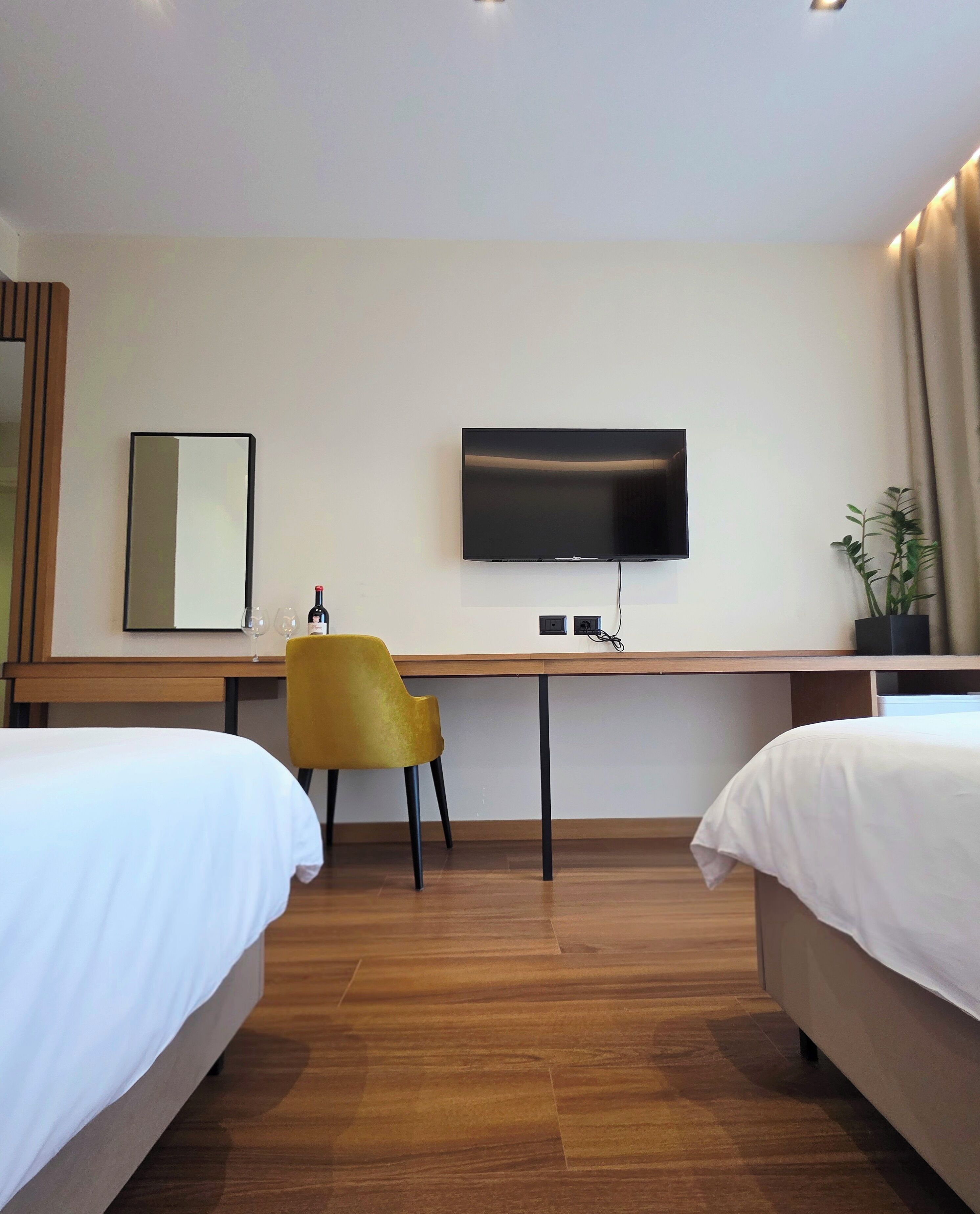 Ett hotellrum med två sängar, ett skrivbord med en stol, en tv och en spegel.