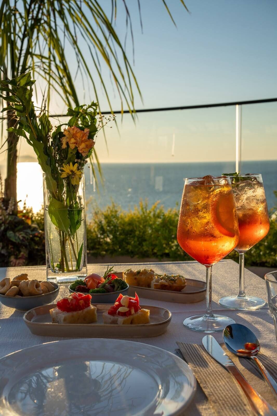 A table set with a glass of iced drink, a vase with flowers, and a plate with food.
