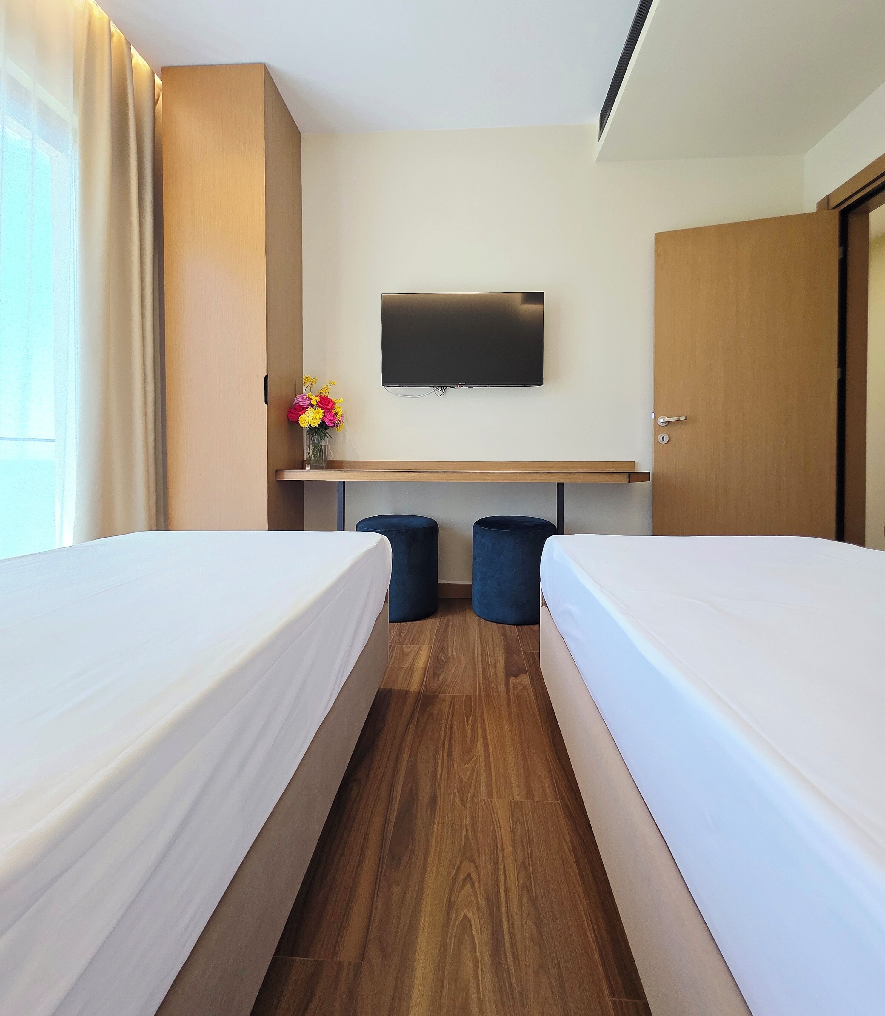 A hotel room with two beds, a TV, a desk, and a window with curtains.