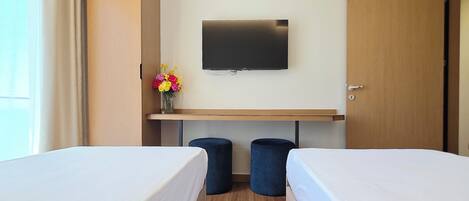 A hotel room with two beds, a TV, a desk, and a window with curtains.