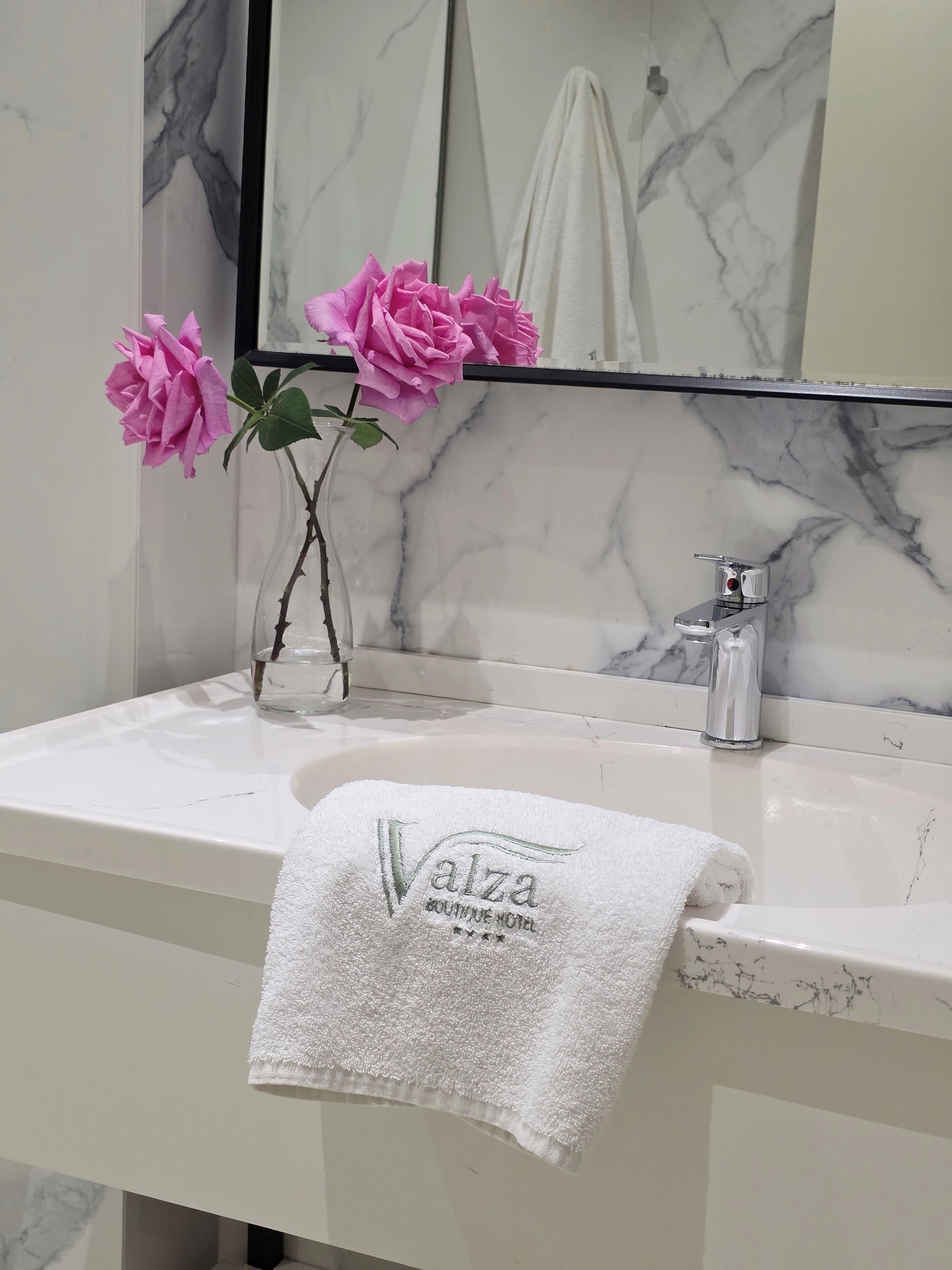 Ein Badezimmer mit Marmorwaschbecken, einem Spiegel und einem Handtuch mit dem Logo des Valza Boutique Hotel.