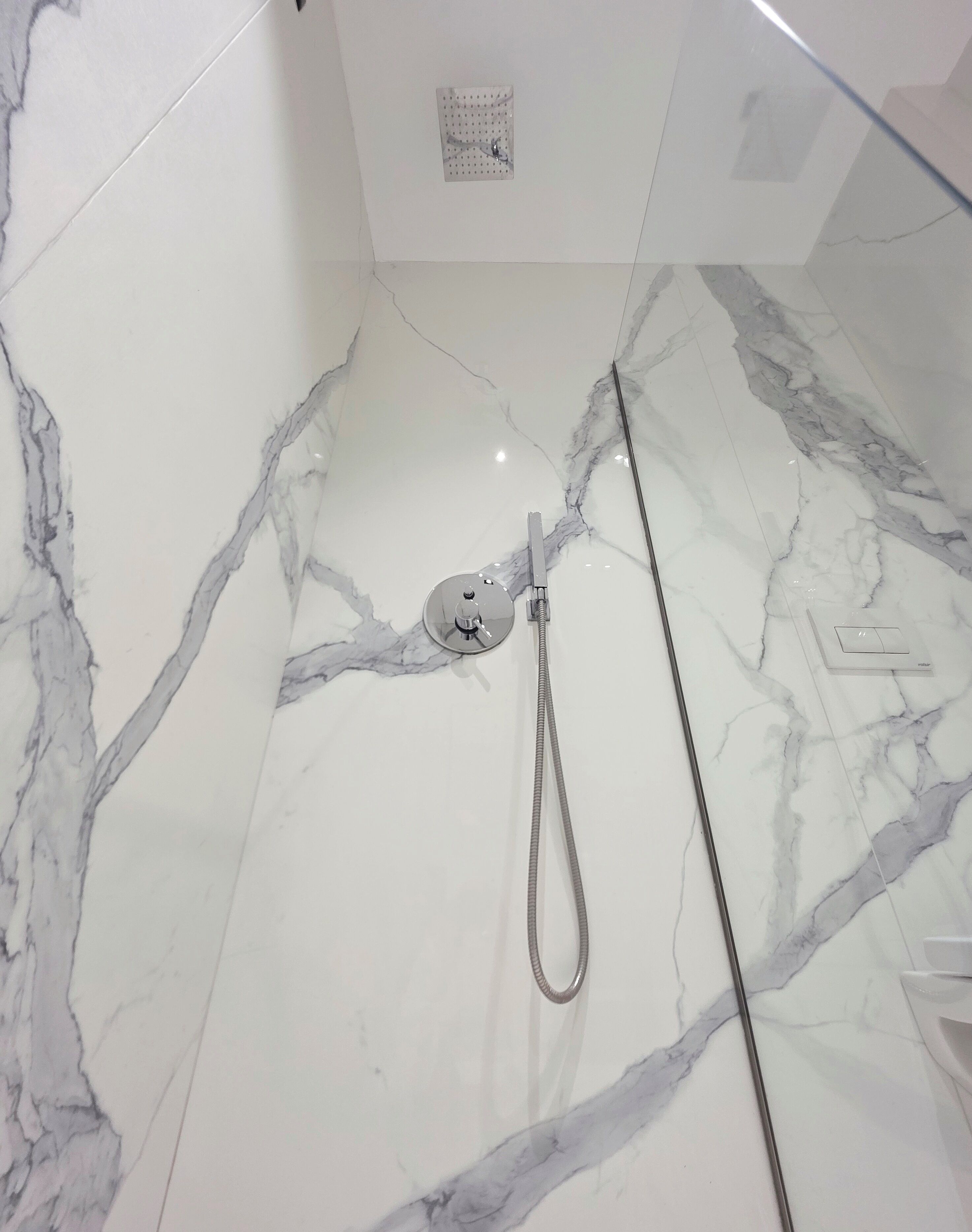 A bathroom with a marble floor, a showerhead, and a control panel.