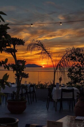 An outdoor dining area with tables and chairs, overlooking a body of water during sunset. - Valza Boutique Hotel (Vlorë)