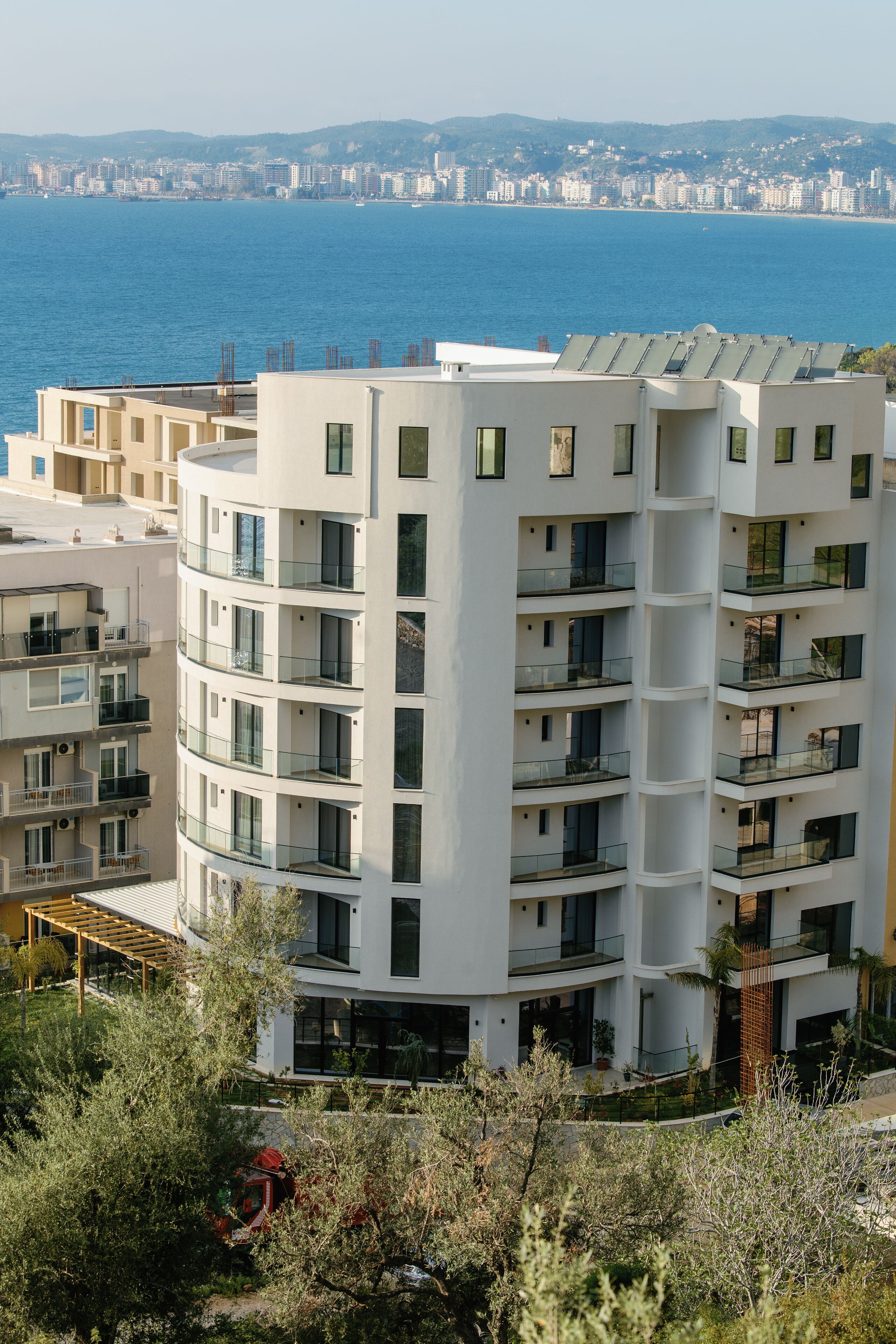 Ein mehrstöckiges Wohngebäude mit Balkonen, Blick auf das Meer und einer Stadtkulisse im Hintergrund.