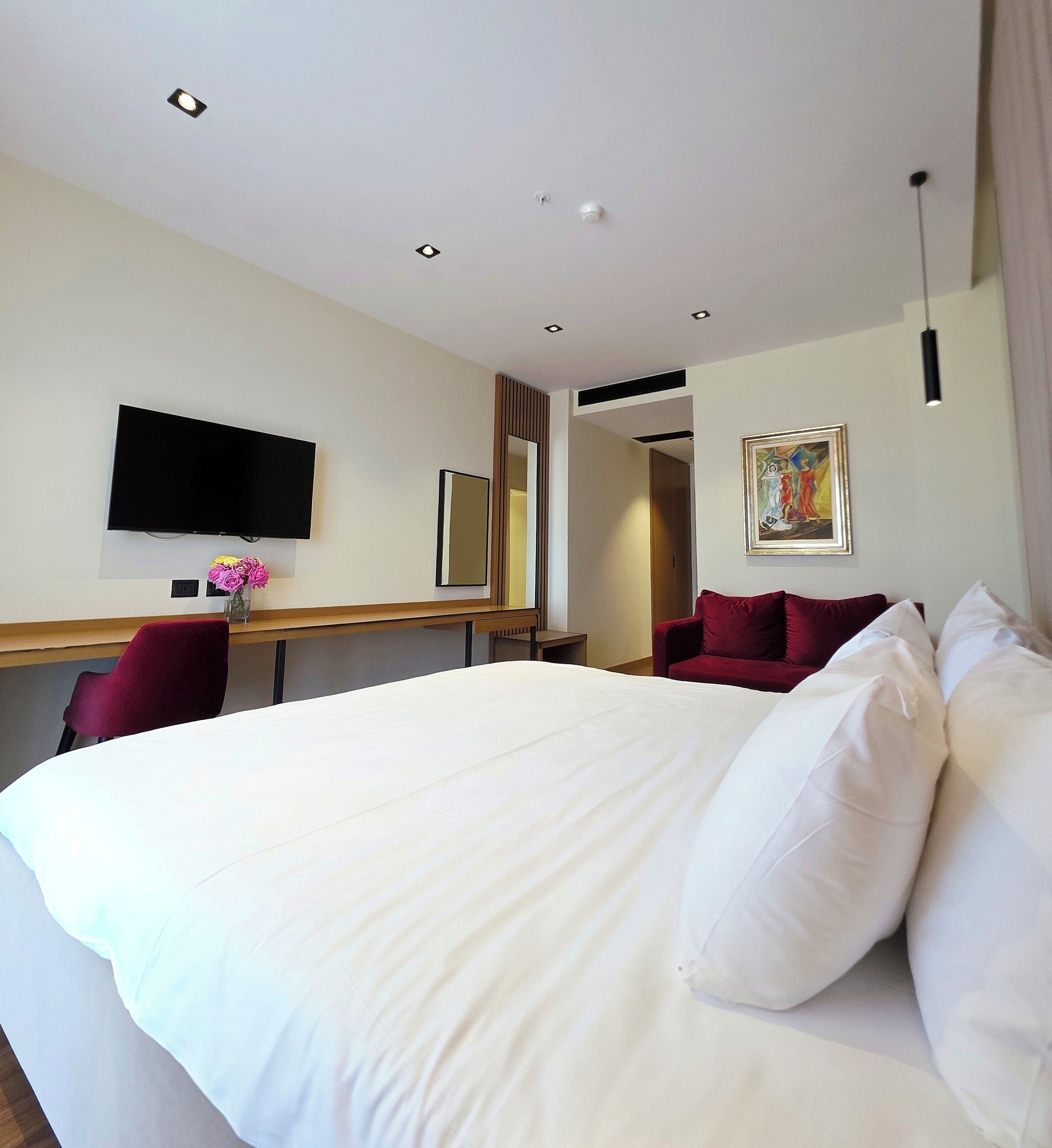 Une chambre d’hôtel avec un grand lit, un bureau doté d’un téléviseur à écran plat, un fauteuil rouge et un tableau accroché au mur.