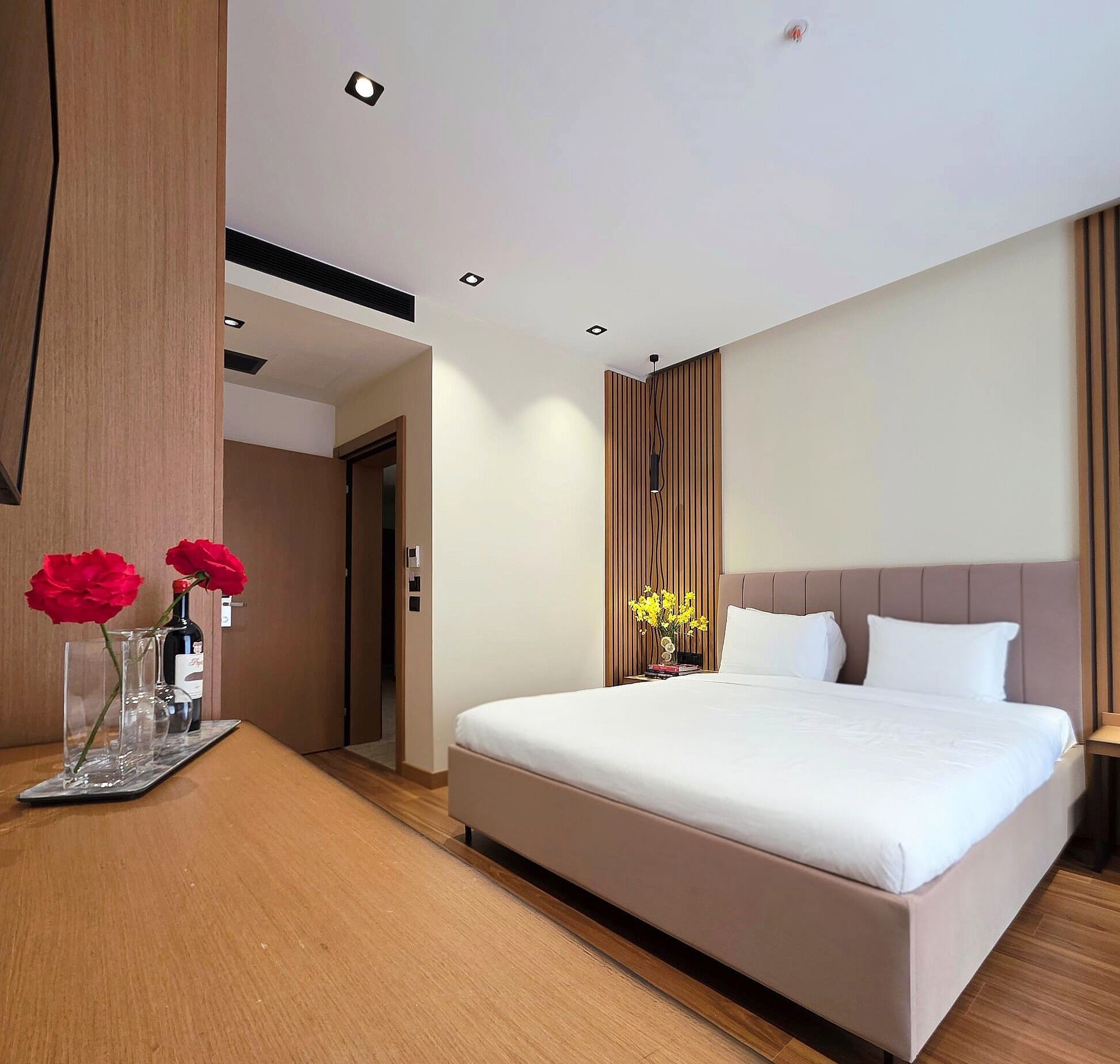 A modern hotel room with a large bed, a wooden desk, and a vase with red flowers.