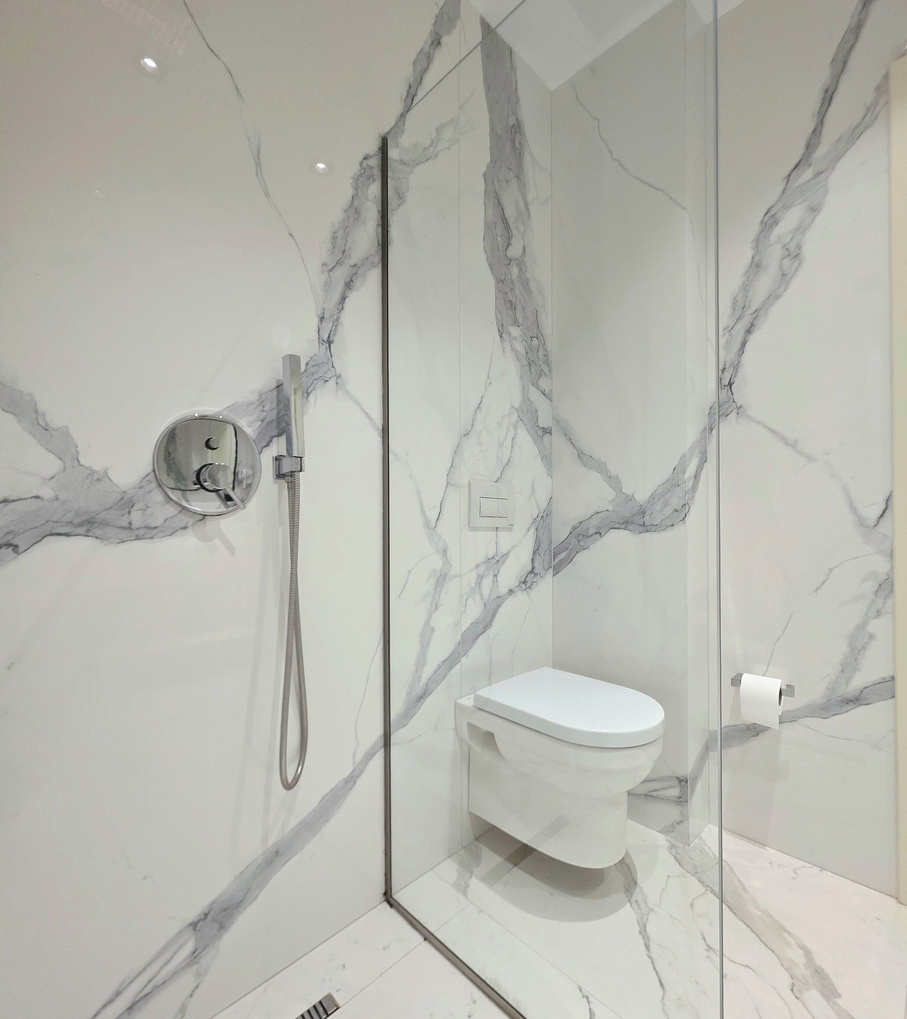 A modern bathroom with a glass-enclosed shower, a white toilet, and marble-patterned walls.