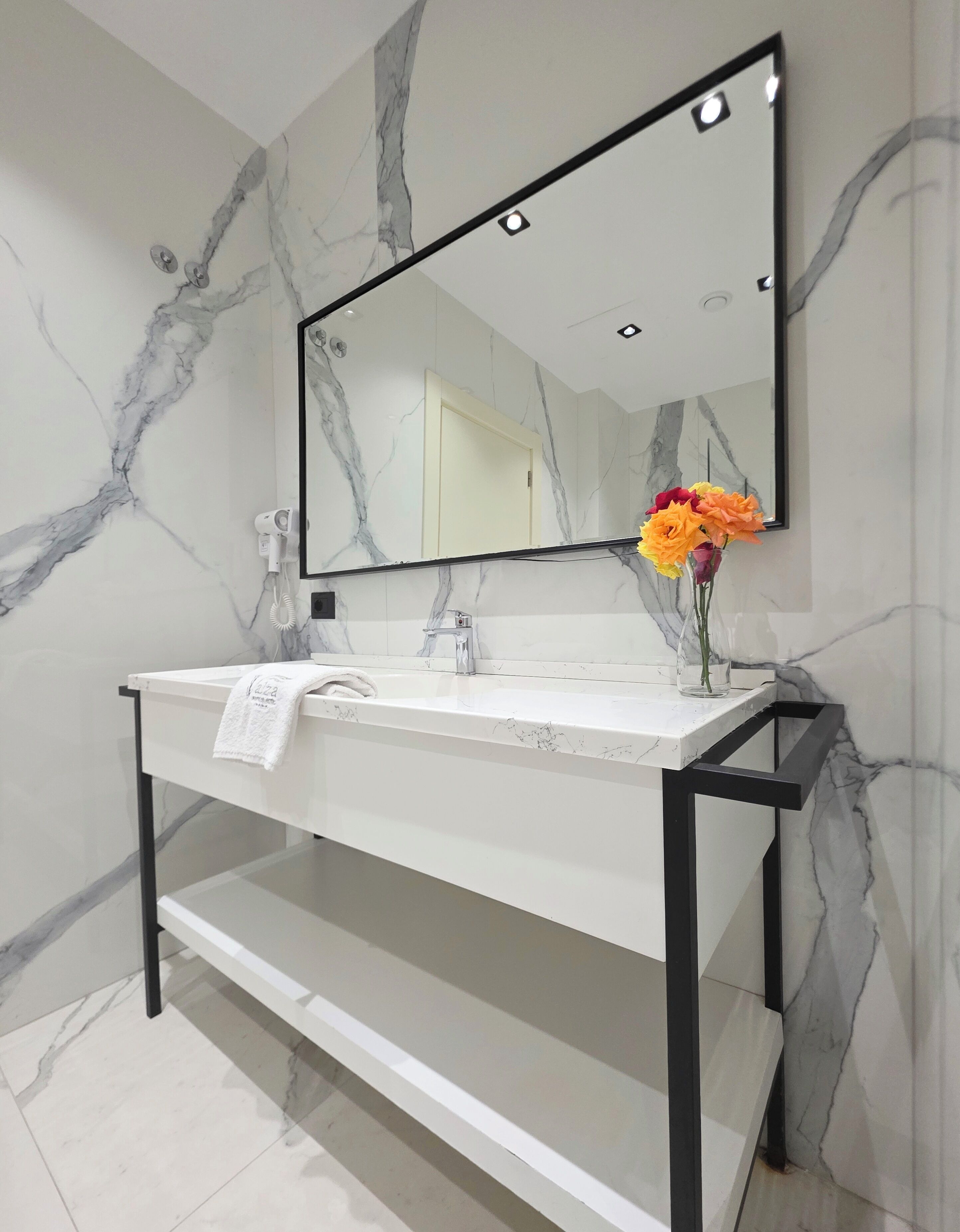 A bathroom with a marble vanity, a large mirror, a towel, and a vase with flowers.