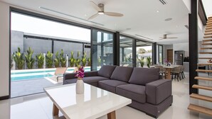 Een moderne woonkamer met een grote hoekbank, een witte salontafel en uitzicht op een zwembad en terras.