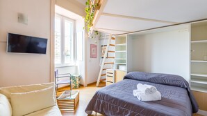 A bedroom with a bed, a TV, a staircase, and a window. - Montemiletto a Panoramic Nest by Napoliapartments (Naples)