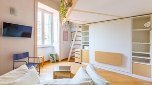 A compact living space with a bed, a TV, a small table, and a staircase leading to a loft area. - Montemiletto a Panoramic Nest by Napoliapartments (Naples)