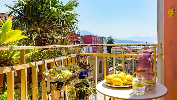A balcony with potted plants, a table with lemons and glasses, and a view of colorful buildings and mountains. - Montemiletto a Panoramic Nest by Napoliapartments (Naples)