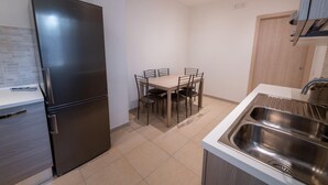 A compact kitchen with a stainless steel refrigerator, a dining table with chairs, and a sink. - Casa Rosa Beige e Blu (Rome)