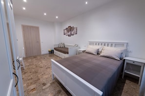 Quarto com cama, mesas de cabeceira, guarda-roupa e porta.