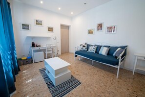 Uma sala de estar moderna com sofá, mesa de centro, escrivaninha com abajur e porta que dá para outro cômodo.