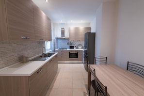 A modern kitchen with wooden cabinets, a stainless steel sink, a built-in oven, and a dining area with a table and chairs. - Casa Rosa Beige e Blu (Rome)