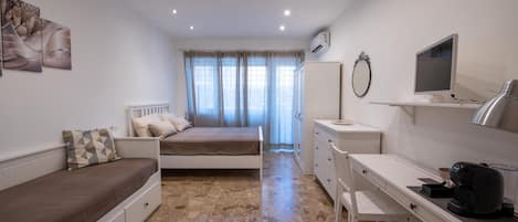 Un dormitorio con cama, escritorio, silla, televisor y aire acondicionado.