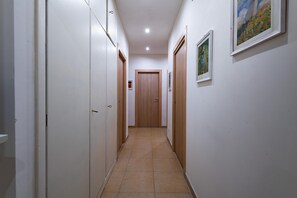 Um corredor estreito com paredes brancas, portas de madeira e chão de azulejos.