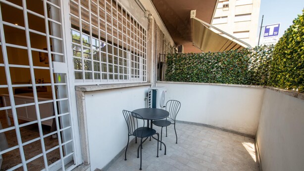 A small outdoor patio area with a table and chairs, a white wall, and a green hedge. - Casa Rosa Beige e Blu (Rome)