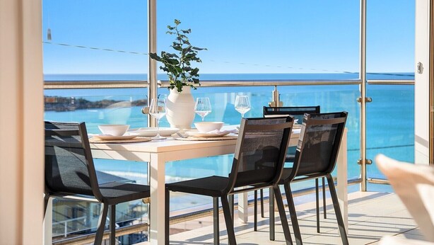 A balcony with a table set for dining, overlooking a clear blue sea. - OUTSTANDING! WHITE HOUSE TASMANIA WINTER SPECIAL MIN STAY 2 NIGHTS TILL OCTOBER. (Boat Harbour Beach)