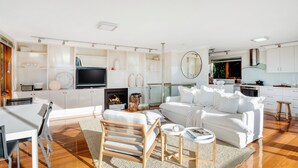 A modern living room with a white sofa, a wooden chair, a TV, and a fireplace. - OUTSTANDING! WHITE HOUSE TASMANIA WINTER SPECIAL MIN STAY 2 NIGHTS TILL OCTOBER. (Boat Harbour Beach)