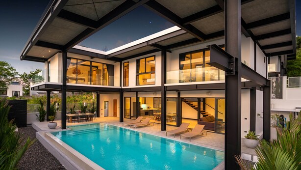 Une maison moderne à deux étages, dotée d’une piscine, de grandes fenêtres et d’un patio couvert.