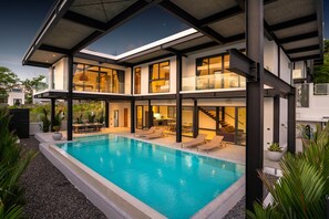 Ein modernes, zweistöckiges Haus mit Swimmingpool, großen Fenstern und einer überdachten Terrasse.