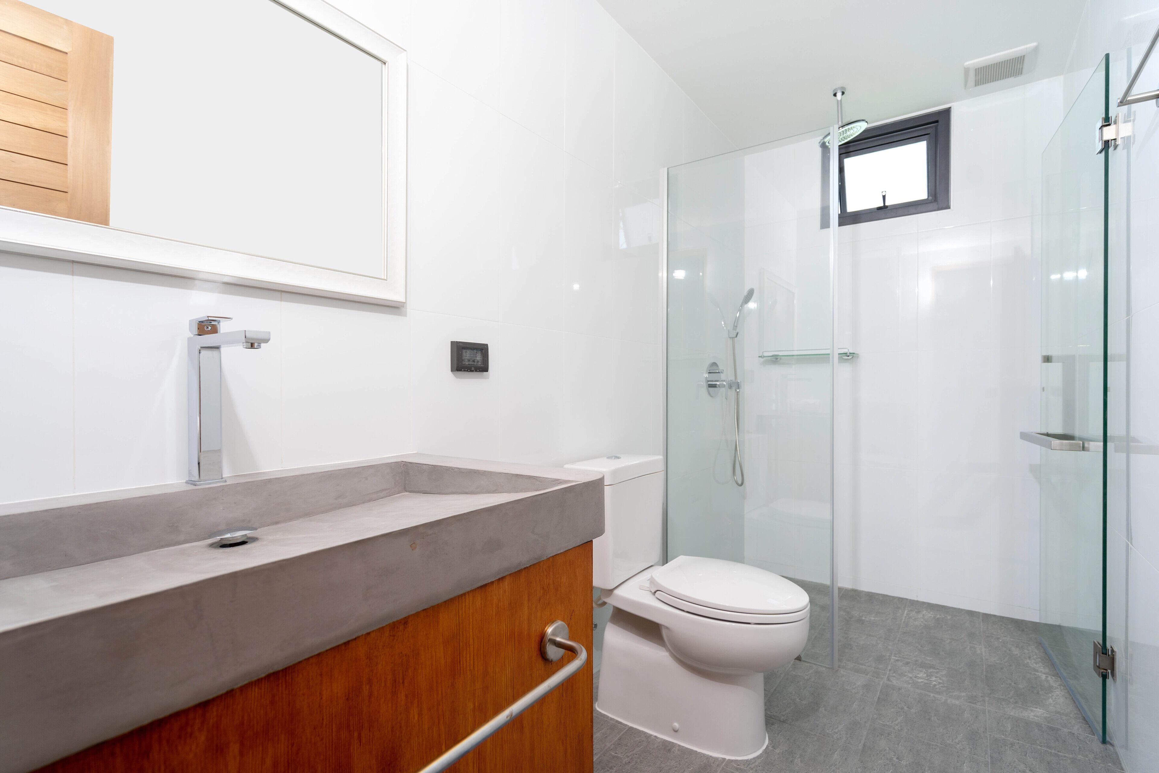 Un baño moderno con cabina de ducha de vidrio, tocador de madera y un inodoro blanco.