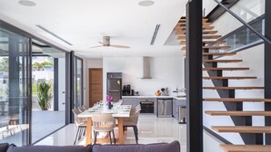 Une cuisine moderne dotée d’appareils électroménagers en acier inoxydable, un coin repas avec une longue table et des chaises, et un escalier avec des marches en bois.