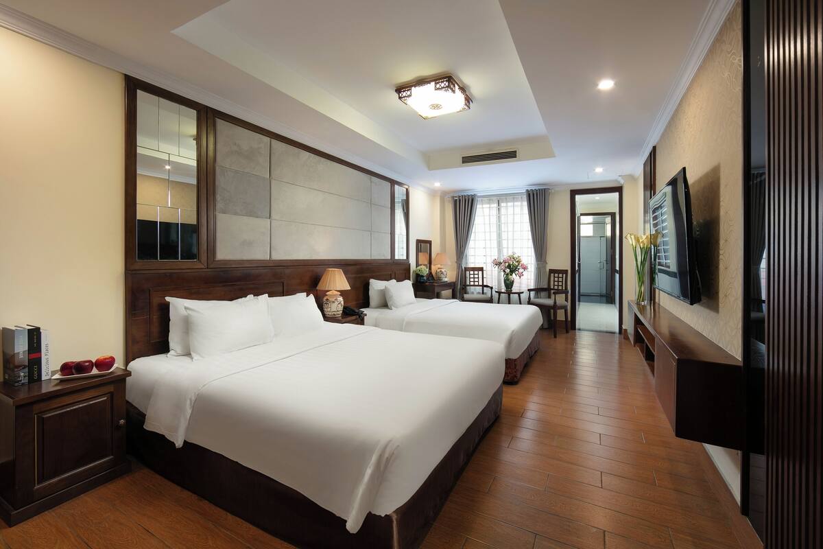 A hotel room with two beds, a TV, a wooden floor, and a large mirror.