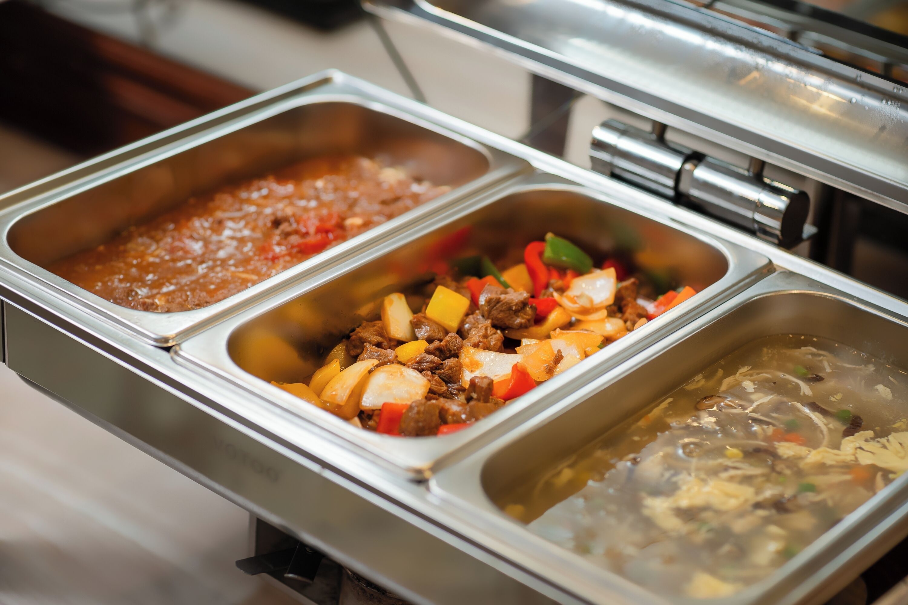 A buffet with various food options including a red sauce, a meat dish with vegetables, and a soup.