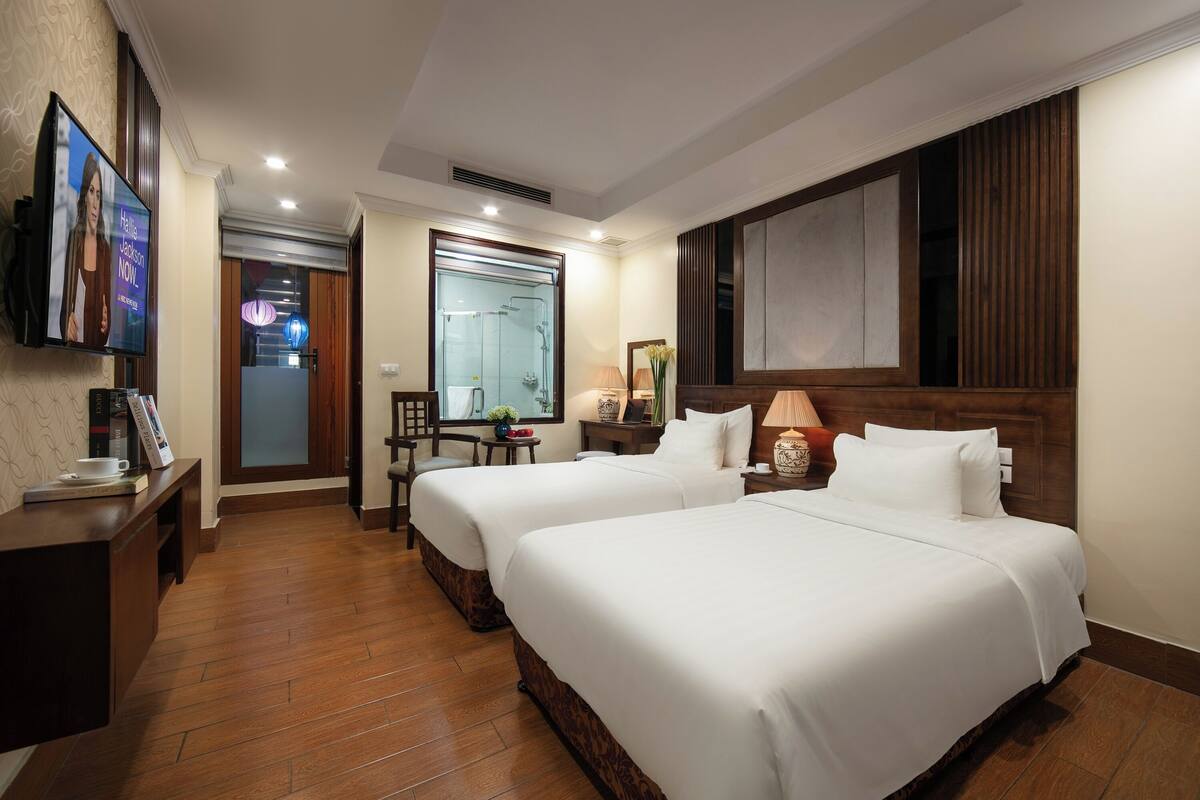 A hotel room with two beds, a desk, a TV, and a bathroom with a shower.