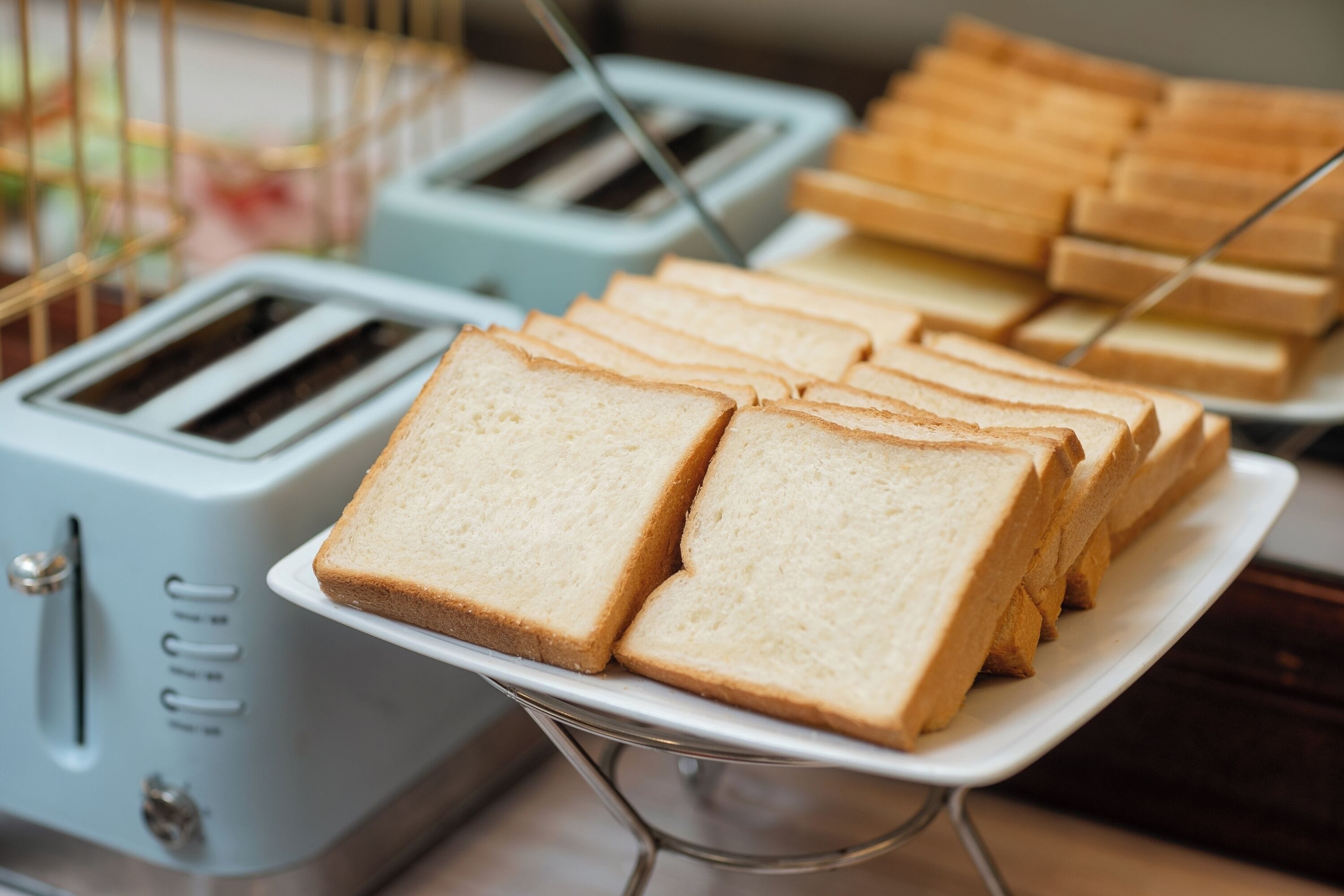 A buffet with multiple toasters and a tray of sliced bread.
