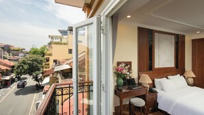 A hotel room with a balcony, a bed, a desk with a laptop, and a vase of flowers. - The West Hotel & Spa (Hanoi)