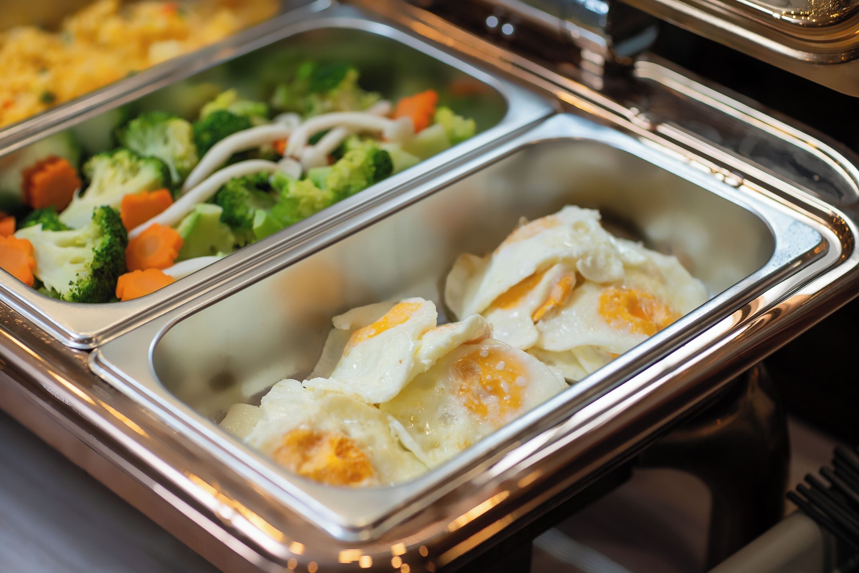A buffet with various food items including eggs, broccoli, and carrots.