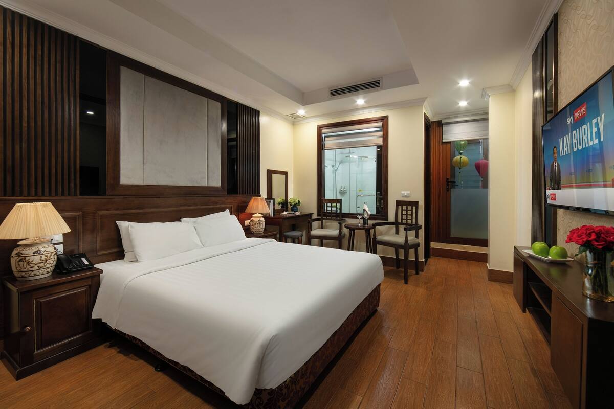 A hotel room with a large bed, a desk with a lamp, a chair, and a mirror.