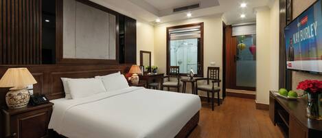 A hotel room with a large bed, a desk with a lamp, a chair, and a mirror.