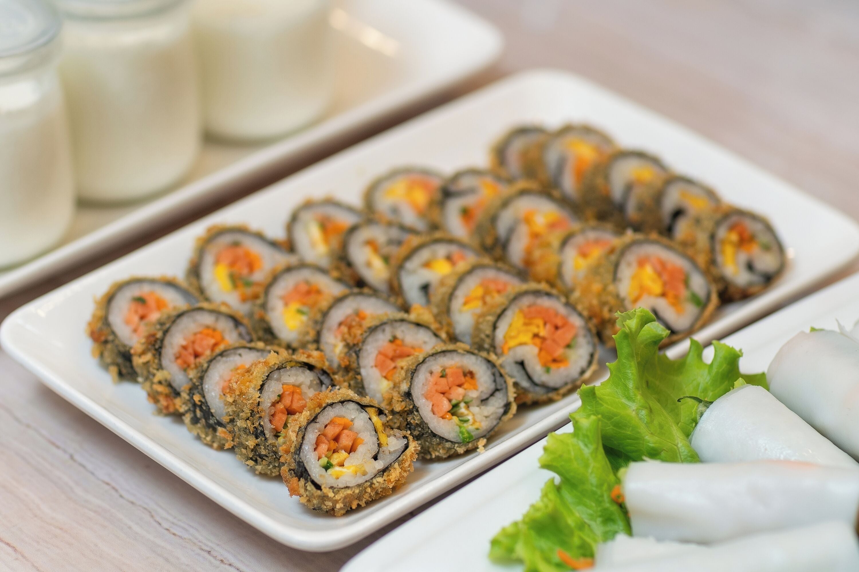 A plate of sushi rolls with a side of fresh lettuce and spring rolls.