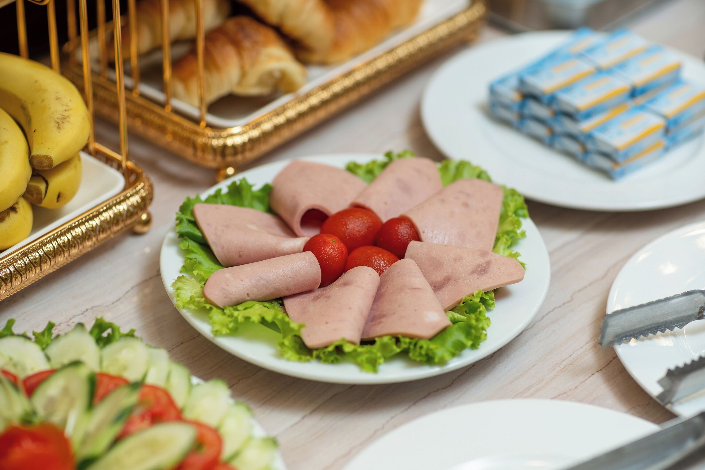Ein Tisch mit verschiedenen Speisen, darunter Schinken, Tomaten und ein Salat.